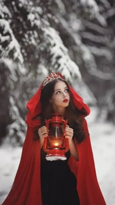 a woman wearing a red cape and holding a lantern in her hands while standing in the snow