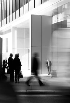 black and white photograph of two people standing on the sidewalk in front of a building