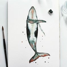 a watercolor painting of a whale on white paper next to some paintbrushes