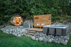 a hot tub sitting next to a wooden barrel in the middle of some rocks and trees