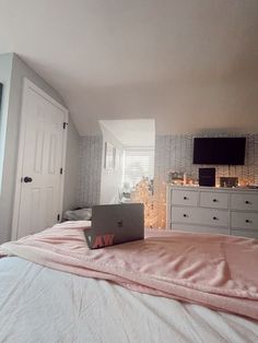 a laptop computer sitting on top of a pink blanket in a bedroom next to a dresser