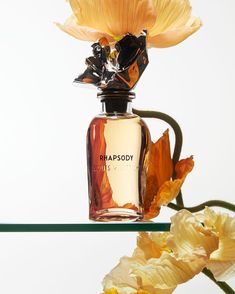 a perfume bottle sitting on top of a glass table next to yellow and orange flowers