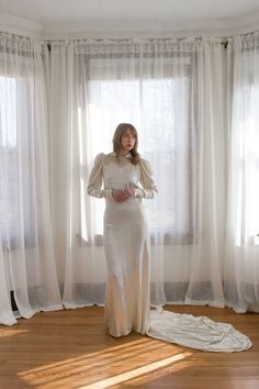 a woman standing in front of a window wearing a long white dress with puffy sleeves