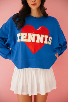 a woman wearing a blue sweatshirt with the word tennis on it and a red heart