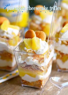 pineapple cheesecake trifles in small clear cups on a wooden table with forks