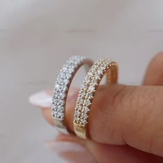 a woman's hand holding two gold and white diamond wedding bands on her finger