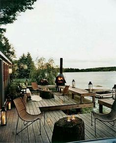 an outdoor deck with chairs, tables and a fire pit on the water's edge