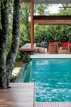 an outdoor pool with chairs and tables next to it in the middle of a forest