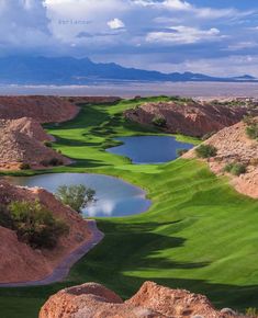 a golf course in the desert with water and rocks around it on a cloudy day