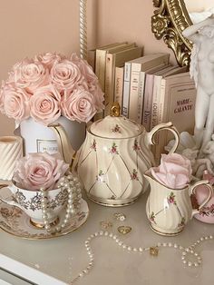 pink roses are in vases, tea cups and books on a white table top