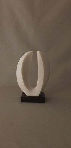 a white sculpture sitting on top of a black stand next to a gray wall in front of it