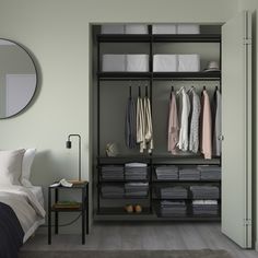 an open closet with clothes hanging on the shelves, and a bed in the background