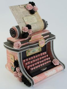 an old fashioned typewriter is decorated with pink roses and black trim, along with paper flowers