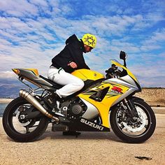 a man sitting on the back of a yellow and black motorbike in front of some water