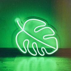 a green neon sign with a leaf on it's side in front of a wall