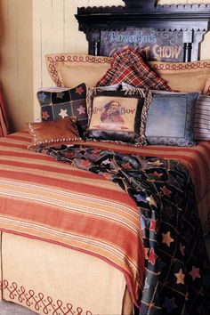 a bed covered in lots of pillows and blankets next to a wall with a clock on it