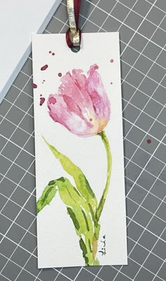 a watercolor painting of a pink tulip on a white card with a red ribbon