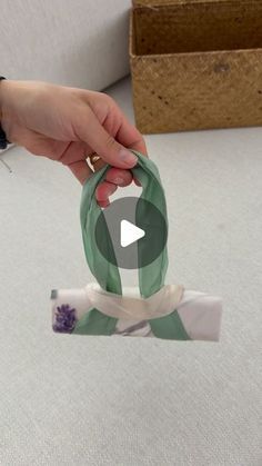 a person holding onto a green and white ribbon with flowers on it, in front of a cardboard box