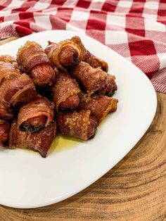 some bacon wrapped in sauce on a white plate next to a red and white checkered table cloth