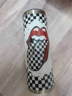 a white and black checkered cup with a red lips on the bottom is sitting on a wood floor