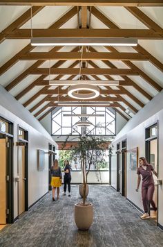 two women walking down the hallway in an office building with large windows and wooden beams