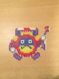 a cross - stitch picture of a colorful fish on a wooden surface, with one eye open