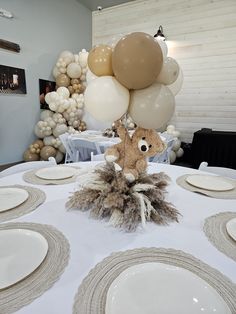 a teddy bear sitting on top of a table surrounded by white plates and silverware