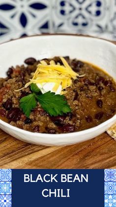 a white bowl filled with black bean chili on top of a wooden table next to bread