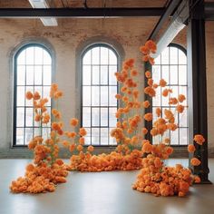 an arrangement of orange flowers in front of two large windows