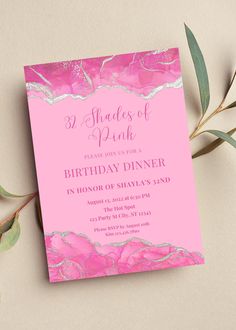 a pink and silver foil birthday party card on top of a table with greenery