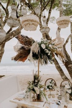 a table set up for an outdoor dinner on the beach with hanging chandeliers