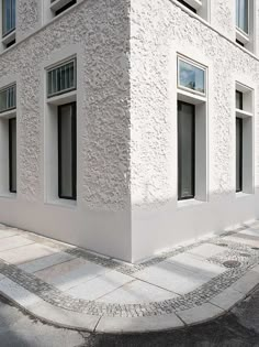 a white building with three windows on the side and a sidewalk in front of it