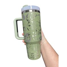 a hand holding a green travel mug with drawings on it and the lid is open