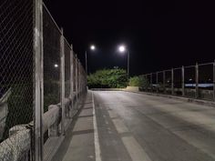 an empty street at night next to a fence