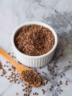 a white bowl filled with flax seeds next to a wooden spoon on a marble surface