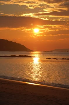 the sun is setting over an ocean with mountains in the distance and water on the beach