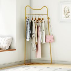 a rack with clothes hanging on it next to a white wall and a pink purse