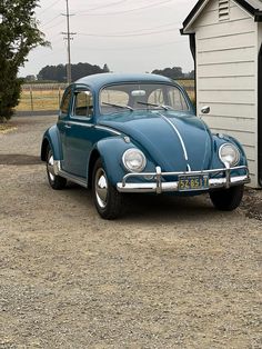 an old blue car parked in front of a white house