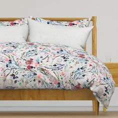 a bed with floral comforter and pillows on top of the headboard, in front of a white wall