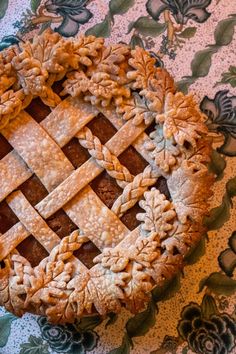 a pie with leaves on it sitting on top of a blue and green table cloth