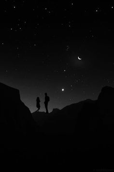 two people standing on top of a mountain at night