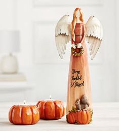 an angel figurine sitting next to three pumpkins on a table with candles