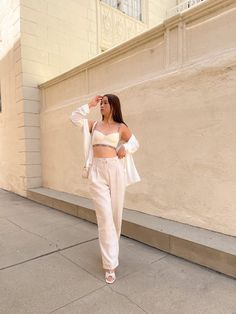 a woman walking down the street wearing white pants and a crop top with an open front jacket