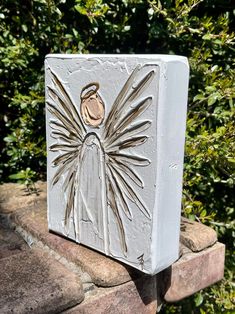 a white box with an angel on it sitting in front of some bushes and trees