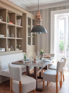 a dining room table surrounded by white chairs and built - in shelving unit behind it