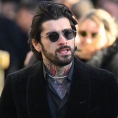 a man with long hair wearing sunglasses and a black suit walking in front of a crowd