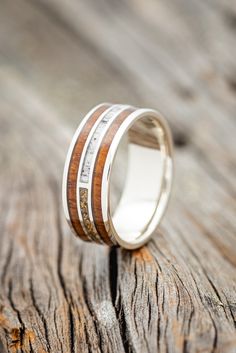 a wedding ring with two bands on top of a piece of wooden planked surface