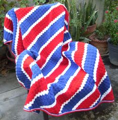 a red, white and blue blanket sitting on top of a chair next to potted plants