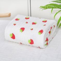 a white blanket with strawberries on it next to a potted plant