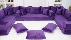 a large purple couch sitting on top of a white floor next to two matching pillows